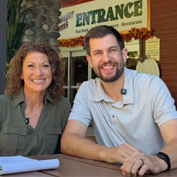A smiling man and woman sitting at an outdoor picnic table in front of a restaurant entrance.