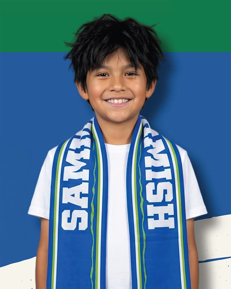 A smiling boy with short black hair wears a white T-shirt and a blue, green, and white scarf that says SOUNDERS. A blue and green background is behind him.